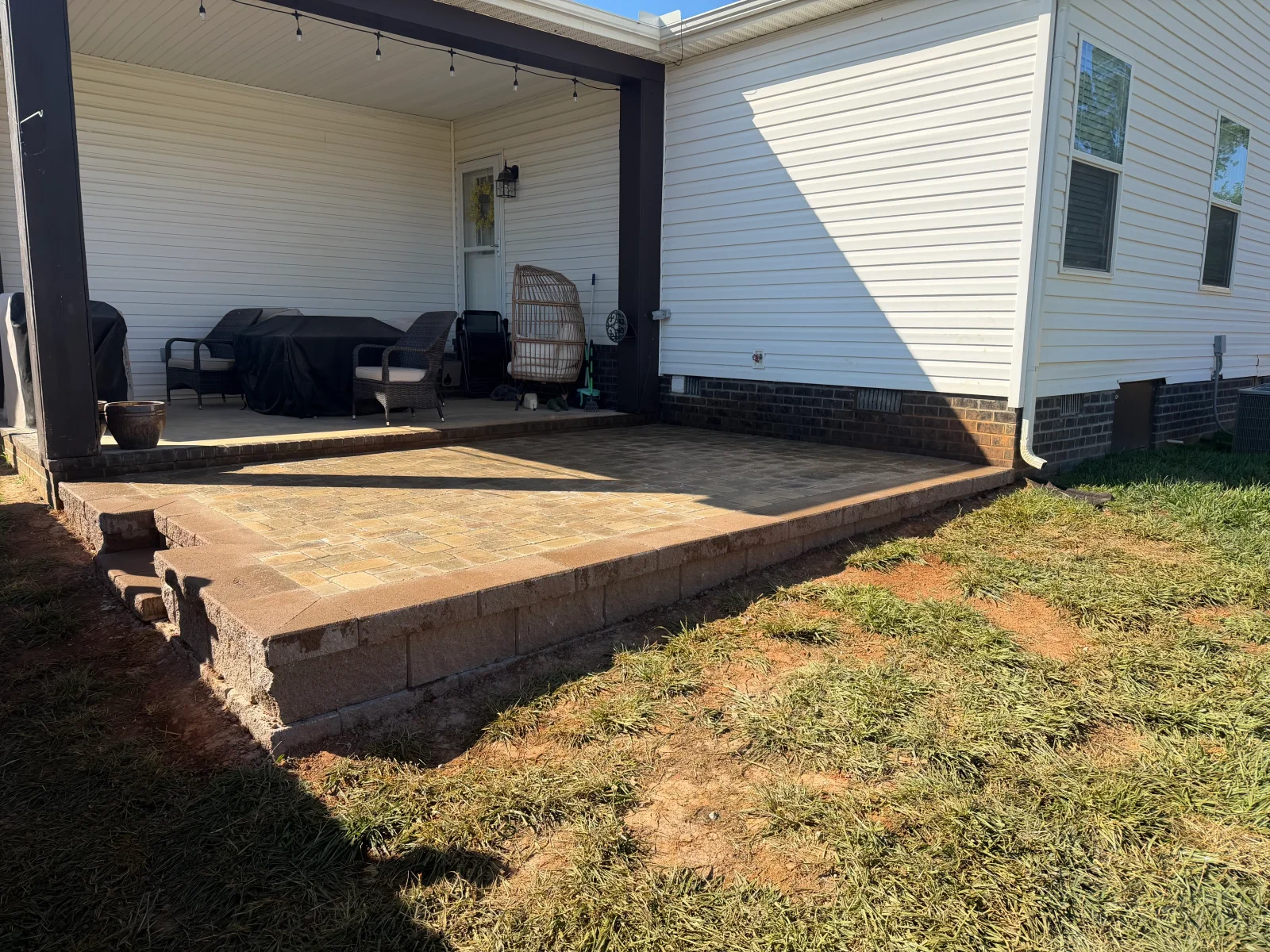 Interlocking paver patio with stacked segmented retaining wall, stone steps, and covered porch with dark steel posts