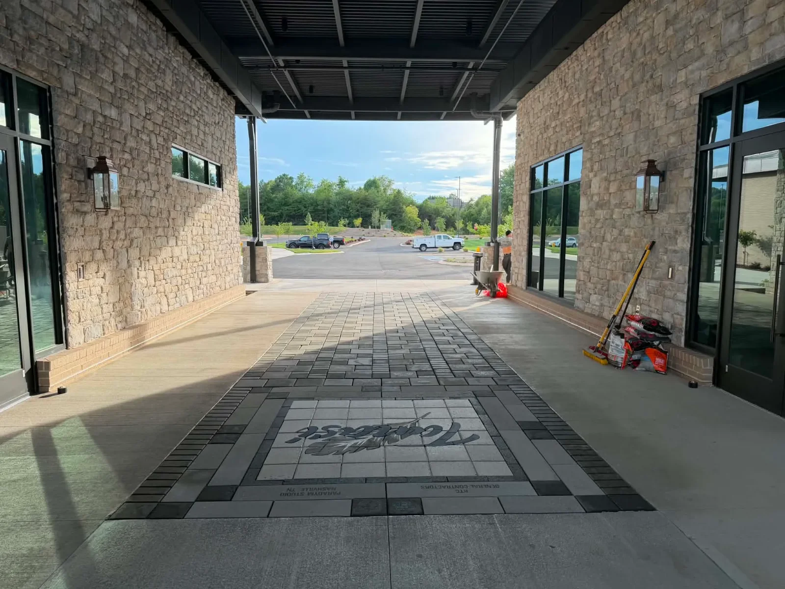 Gray concrete paver entryway with a custom script logo medallion under a covered walkway beside stone-clad walls