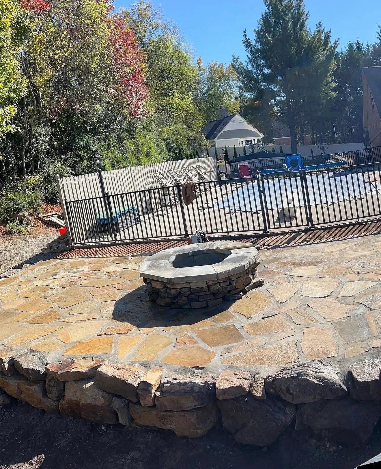 Irregular flagstone patio with stone fire pit and dry-stacked stone retaining wall beside a black aluminum pool fence