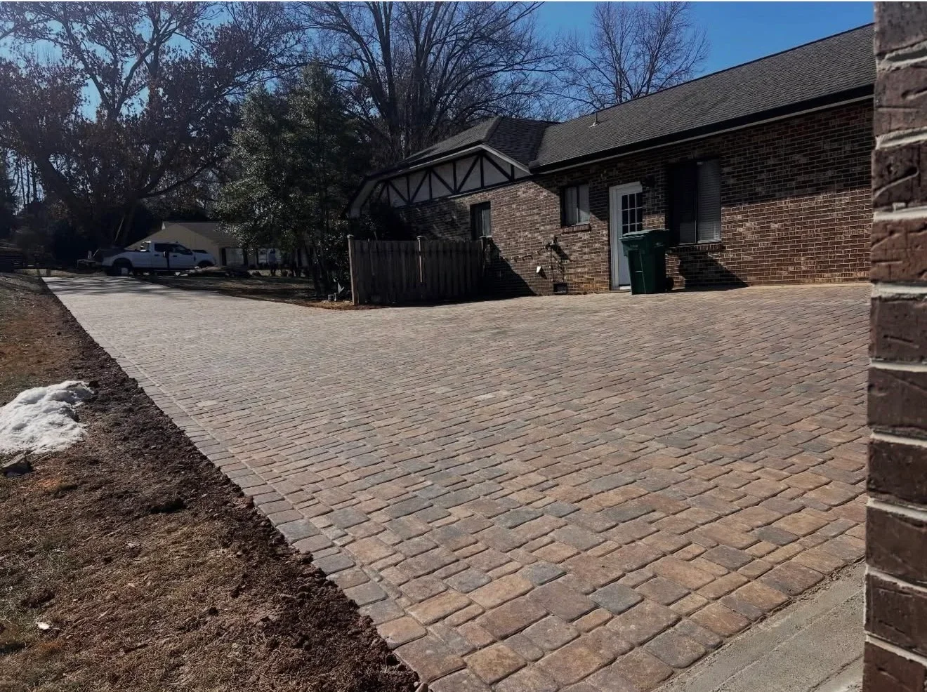 Multi-toned concrete paver driveway in tan, brown, and gray laid in running bond beside a brick home